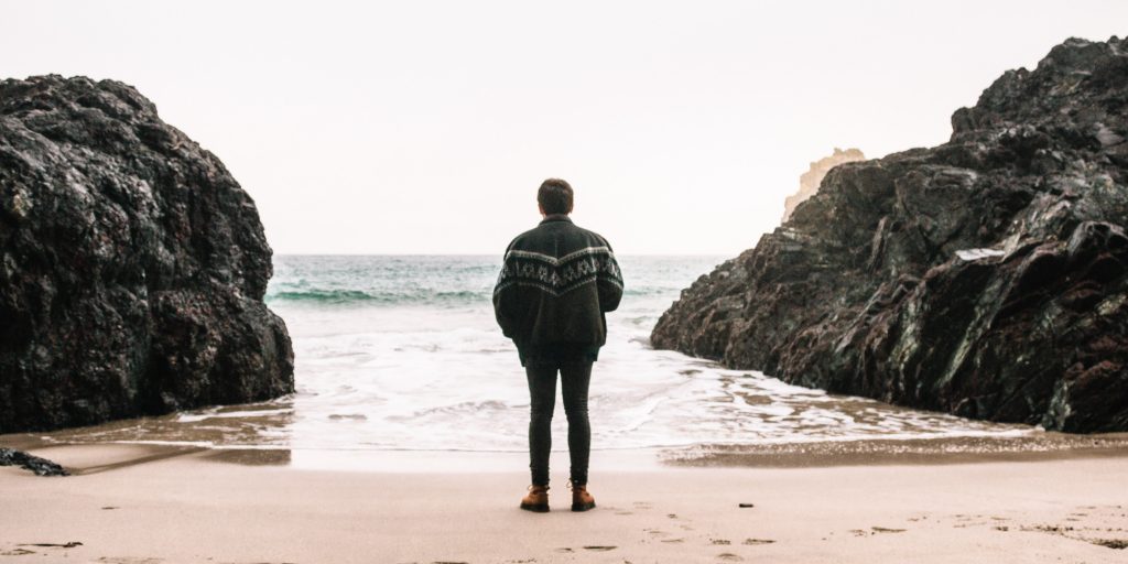 Photograph of a figure on the beach looking at the sea.